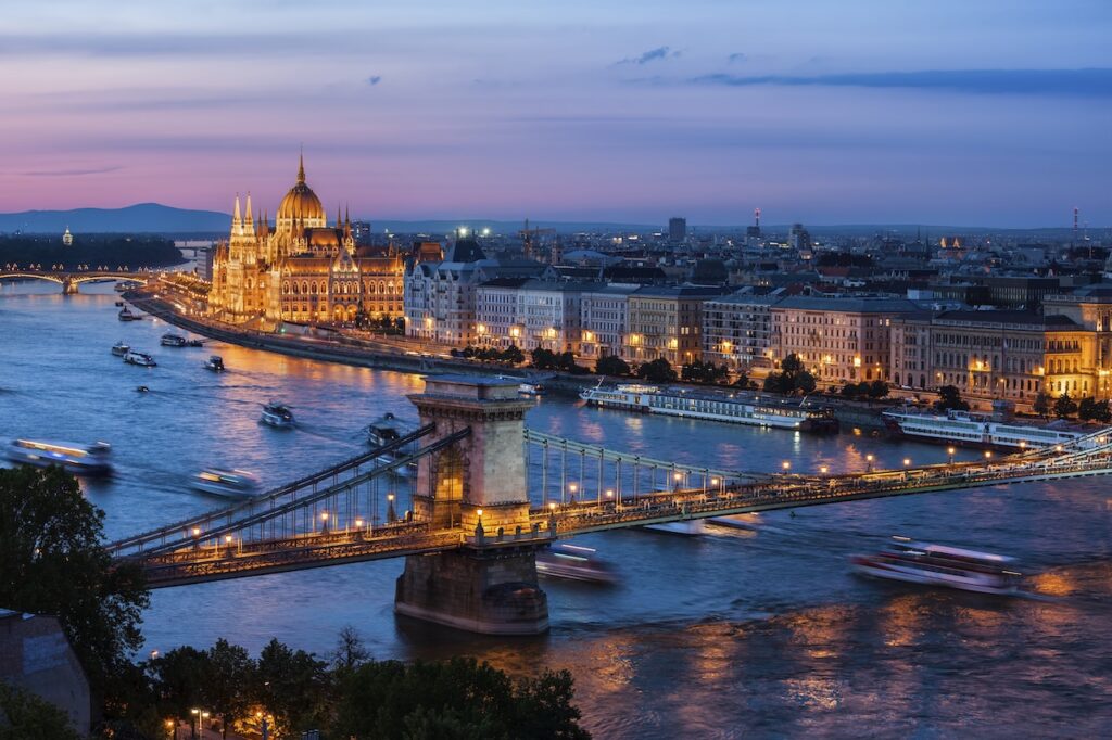 Dramatic night view of Budapest with the Hungarian Parliament Building and the Chain Bridge fully illuminated along the Danube River.