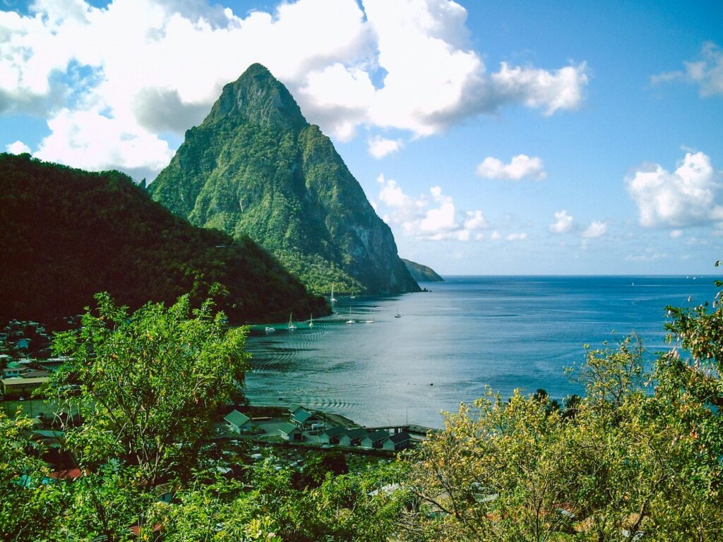 A lush, green mountain peak rises dramatically from the Caribbean Sea under a blue sky, showcasing the natural beauty of the island of Saint Lucia.