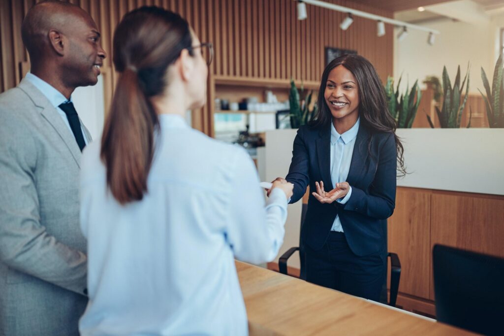 A woman in a business suit shakes hands with colleagues, showing professional collaboration at a modern, tech-driven travel company.