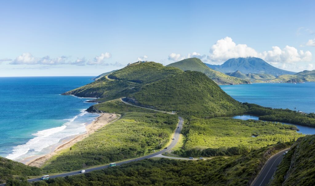 Breathtaking aerial view of a scenic coastal road winding through green mountains and hills, highlighting adventure travel and stunning Caribbean island views.