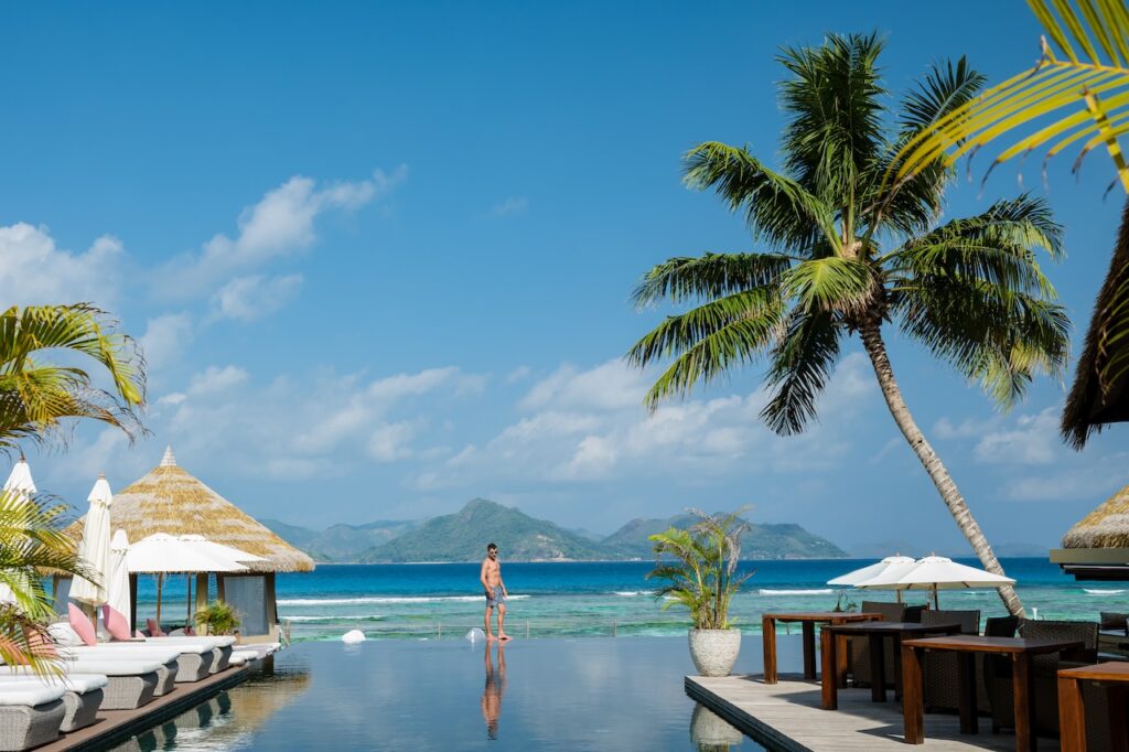 Man enjoying the view from a luxury resort infinity pool, highlighting a high-end tropical beach vacation and exclusive accommodations.