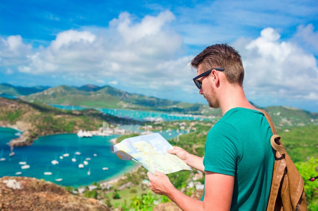 Man reading a map on a high viewpoint overlooking a scenic tropical island and bay, highlighting travel planning and exotic destination exploration.