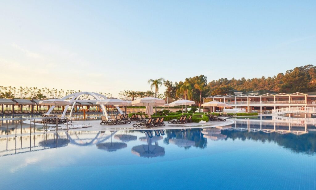 A wide, tranquil blue swimming pool at a luxury resort, surrounded by lounge chairs and white umbrellas, reflecting the high standards and exclusive amenities often associated with the Four Seasons loyalty program.