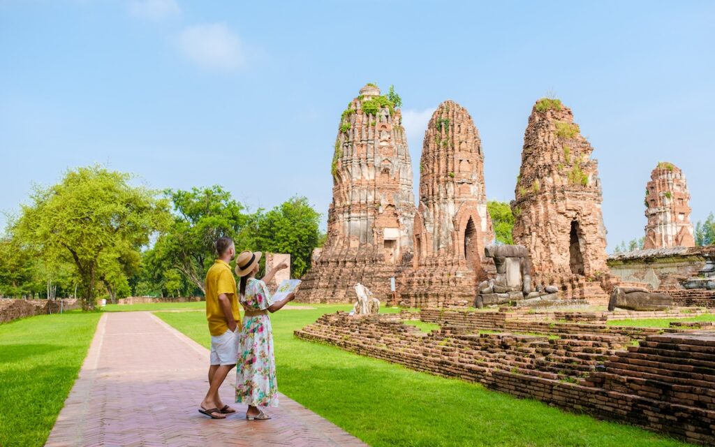 A couple reviewing a map at the expansive ruins of an ancient Thai temple, emphasizing historical heritage exploration during a luxury trip.