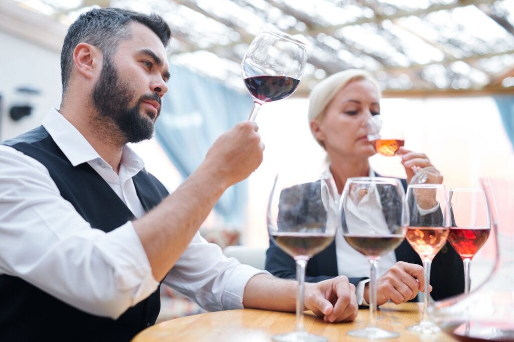 Sommelier and woman engaged in professional wine tasting, examining a glass of red wine, highlighting luxury food, beverage, and dining experiences.