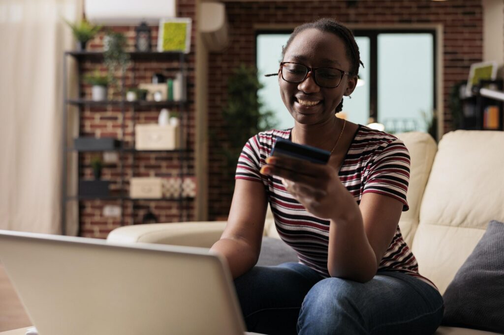A woman smiles on a couch using her laptop and Citi credit card, showing how easy it is to manage accounts and redeem rewards.