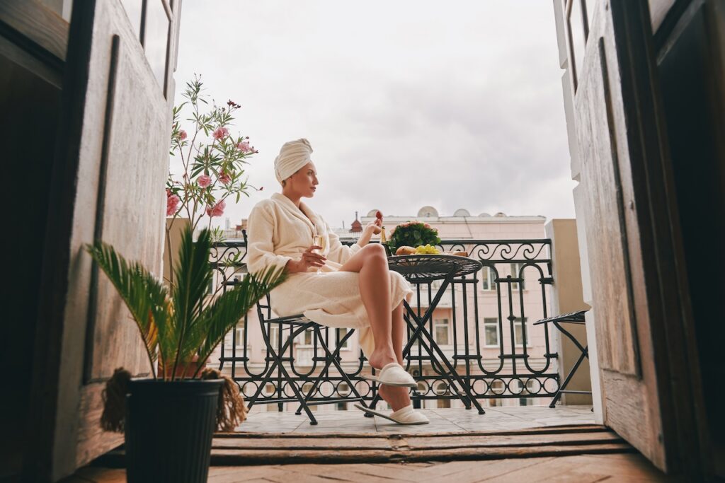 Guest relaxing in a luxurious bathrobe on a wrought-iron balcony with champagne, representing the ultimate comfort and private luxury experience at the island hotel and spa.
